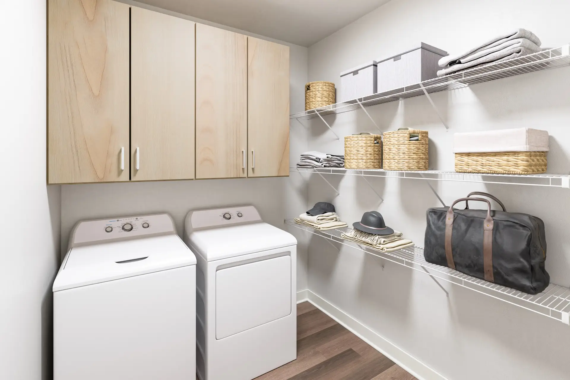 A modern laundry room with a white washer and dryer, light wood-like cabinets above, open wire shelves, and a wood-look pattern floor.