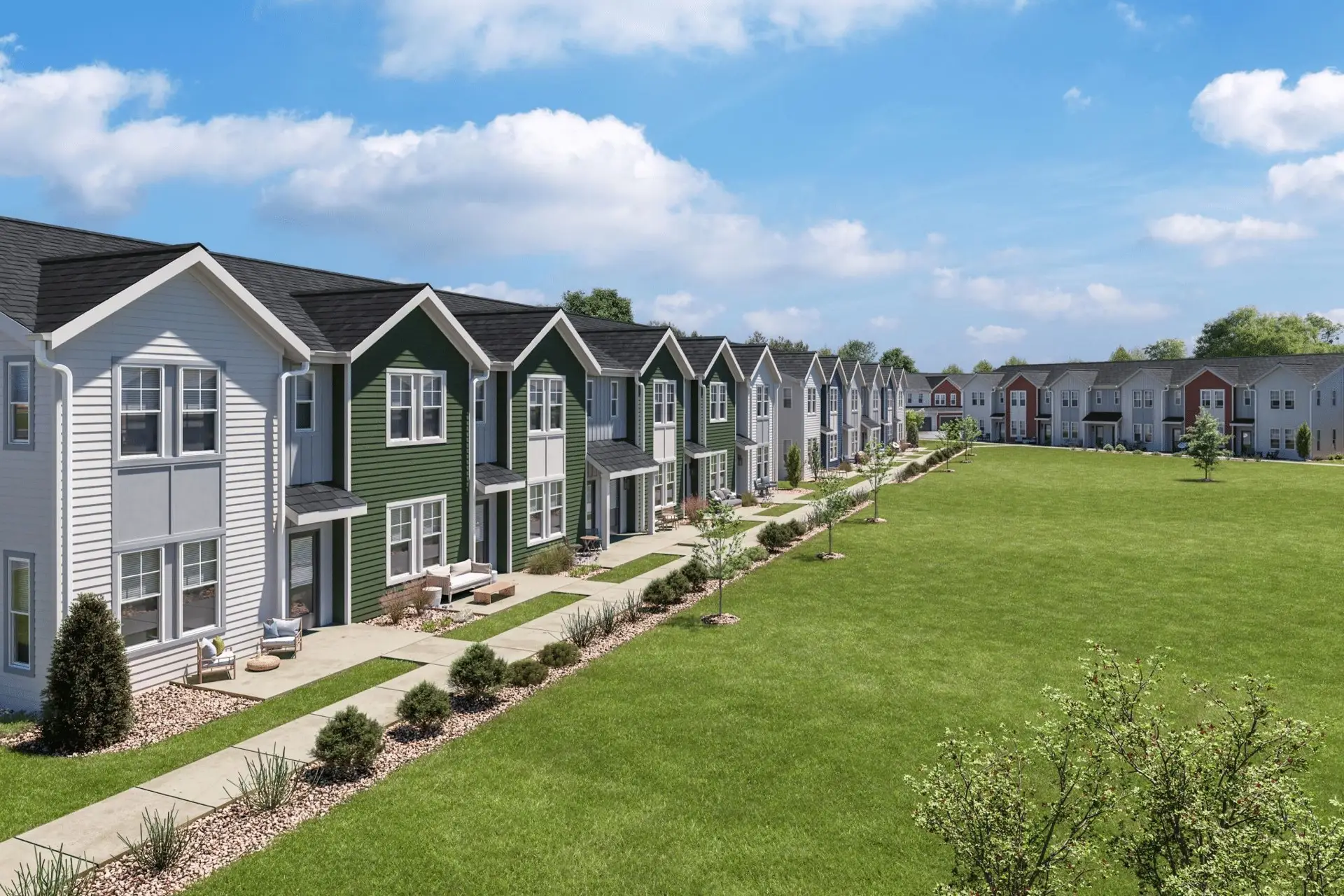 Row of modern townhouses with green lawns, sidewalks, and landscaped greenery on a sunny day beneath a blue sky with clouds.